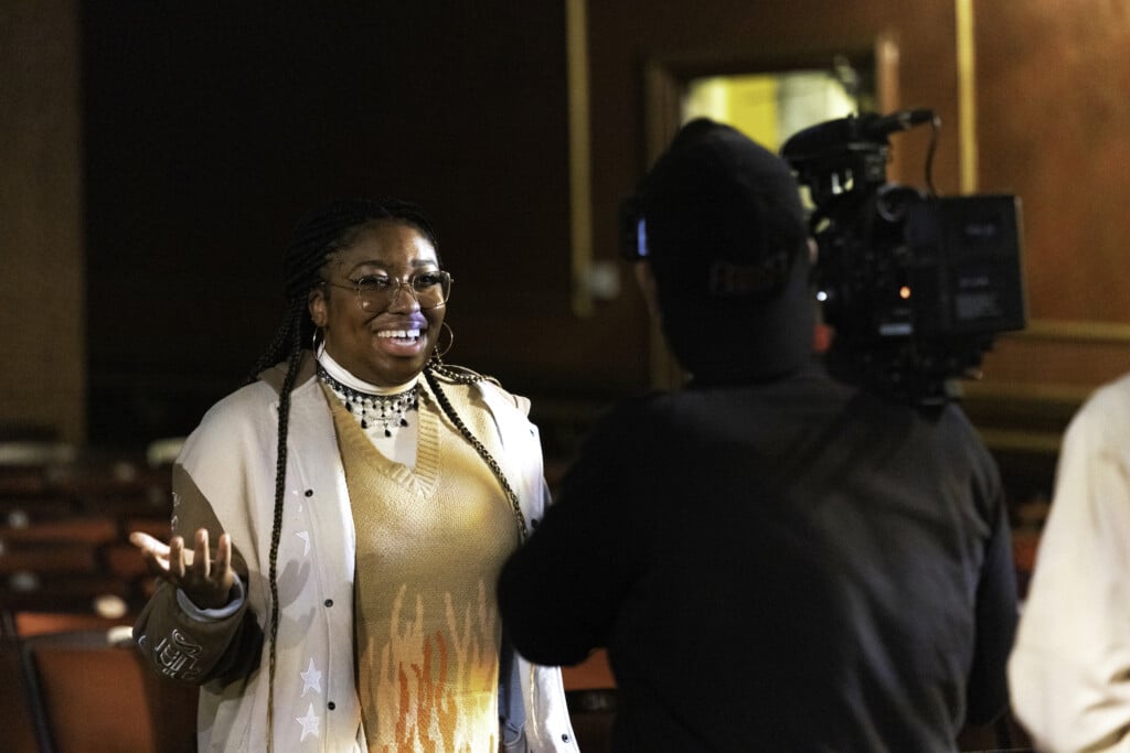 Photo of a camera man filming a woman as she speaks to the camera