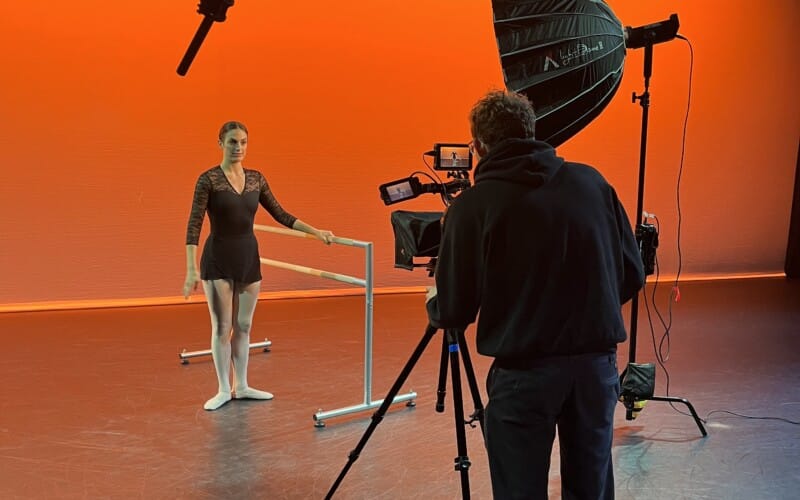 Cameraman filming a Ballerina with Ballet Bar in an Orange Studio