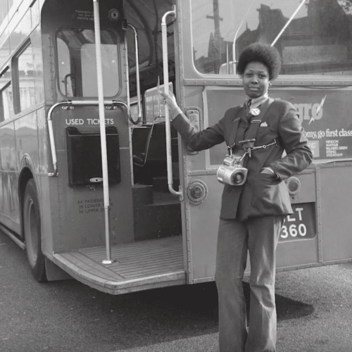 Black and white photograph of a black female ticket conductor next to a vintage double decker bus for the Museum of London 'Last Chance to See' exhibit
