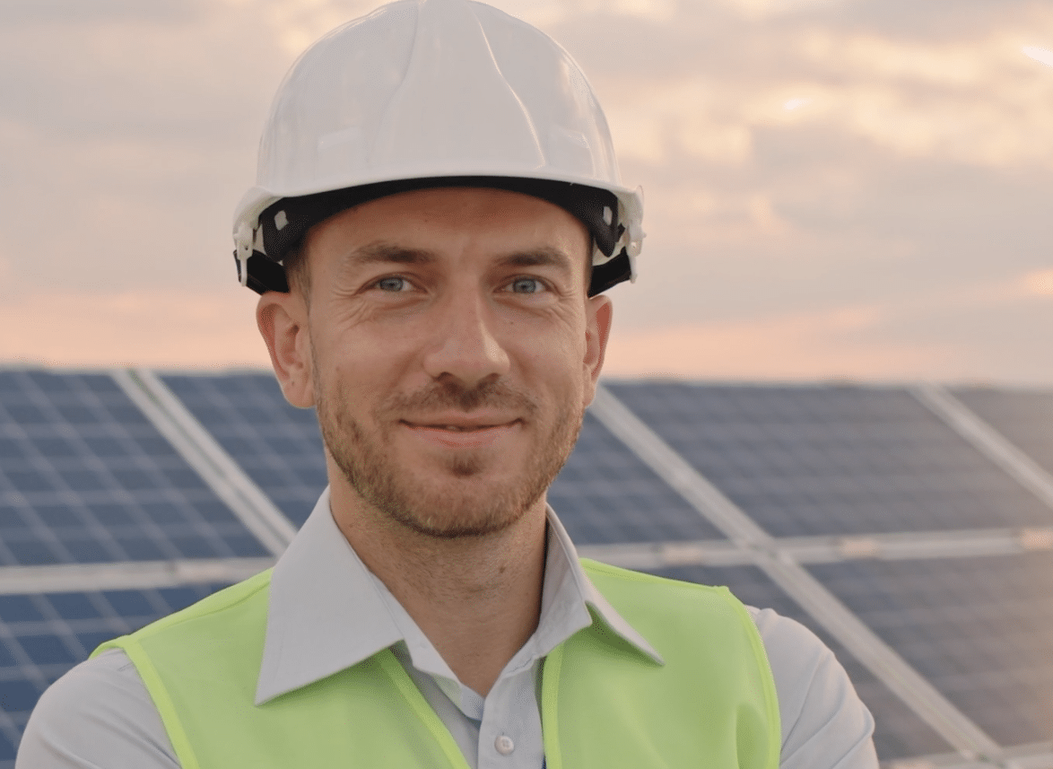 Taylor Hopkinson worker in a hard hat stood in front of a wall of solar panels and smiling at the camera