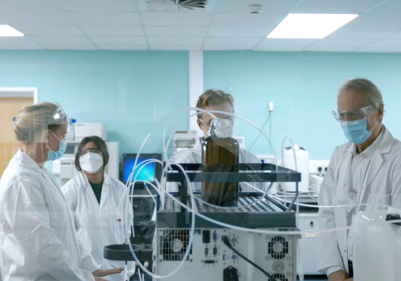 Four scientists in white lab coats gathered around a chemical experiment in a lab