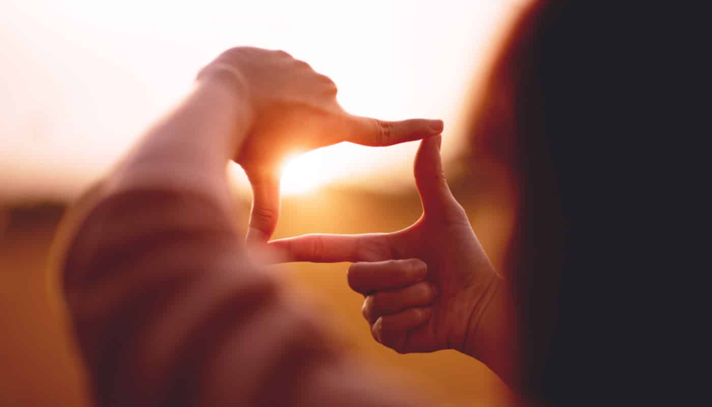 Woman holds up two hands to frame a landscape