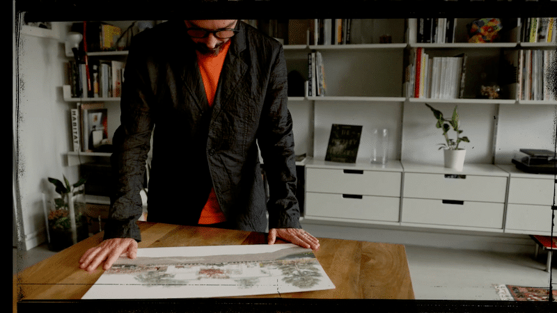 Artist in booklined room looks at illustrated plans for V and A Dundee